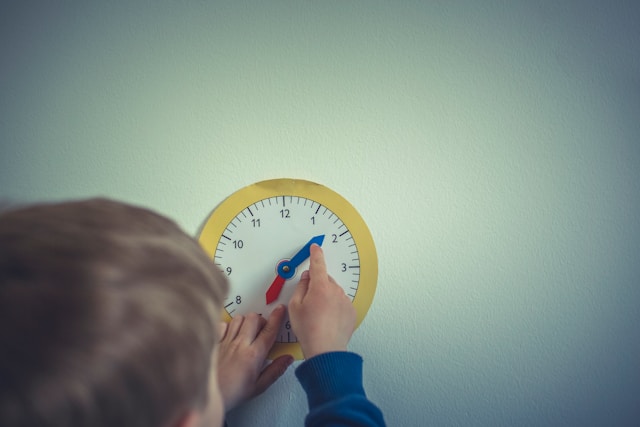 おもちゃの時計の針を動かして、時間を確認する子どもの後ろ姿